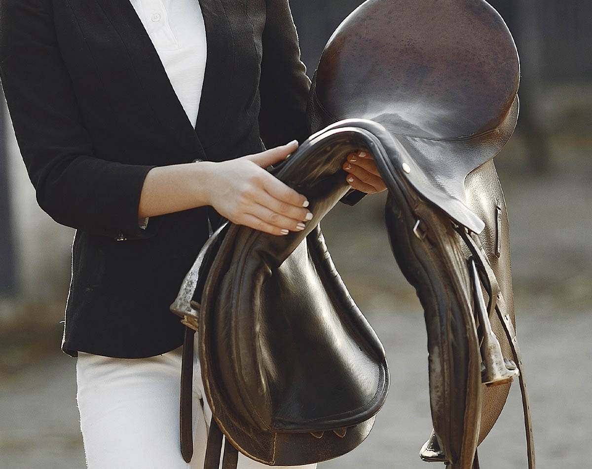 Close em mulher segurando sela com roupa formal típica de dias de provas e competições